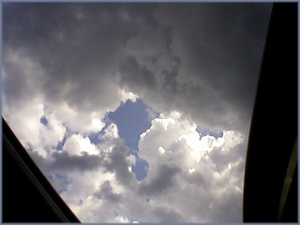 clouds seen through an undefined opening, a window or door, with a hole in the clouds through which the blue sky is seen
