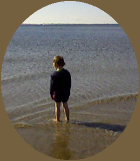 image of a young boy standing in shallow ocean water with small ripples, looking down into the water
